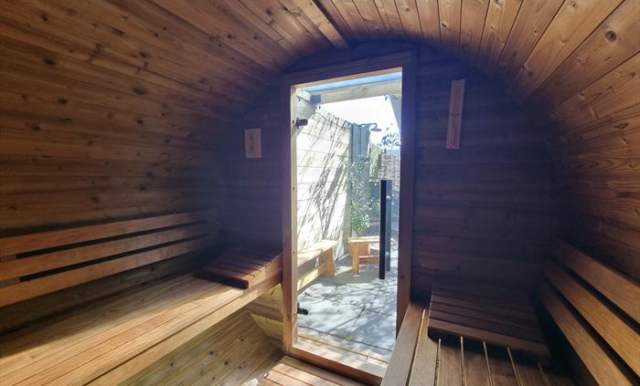 Inside a wooden barrel shaped sauna with wooden benches and a glass door to the outside